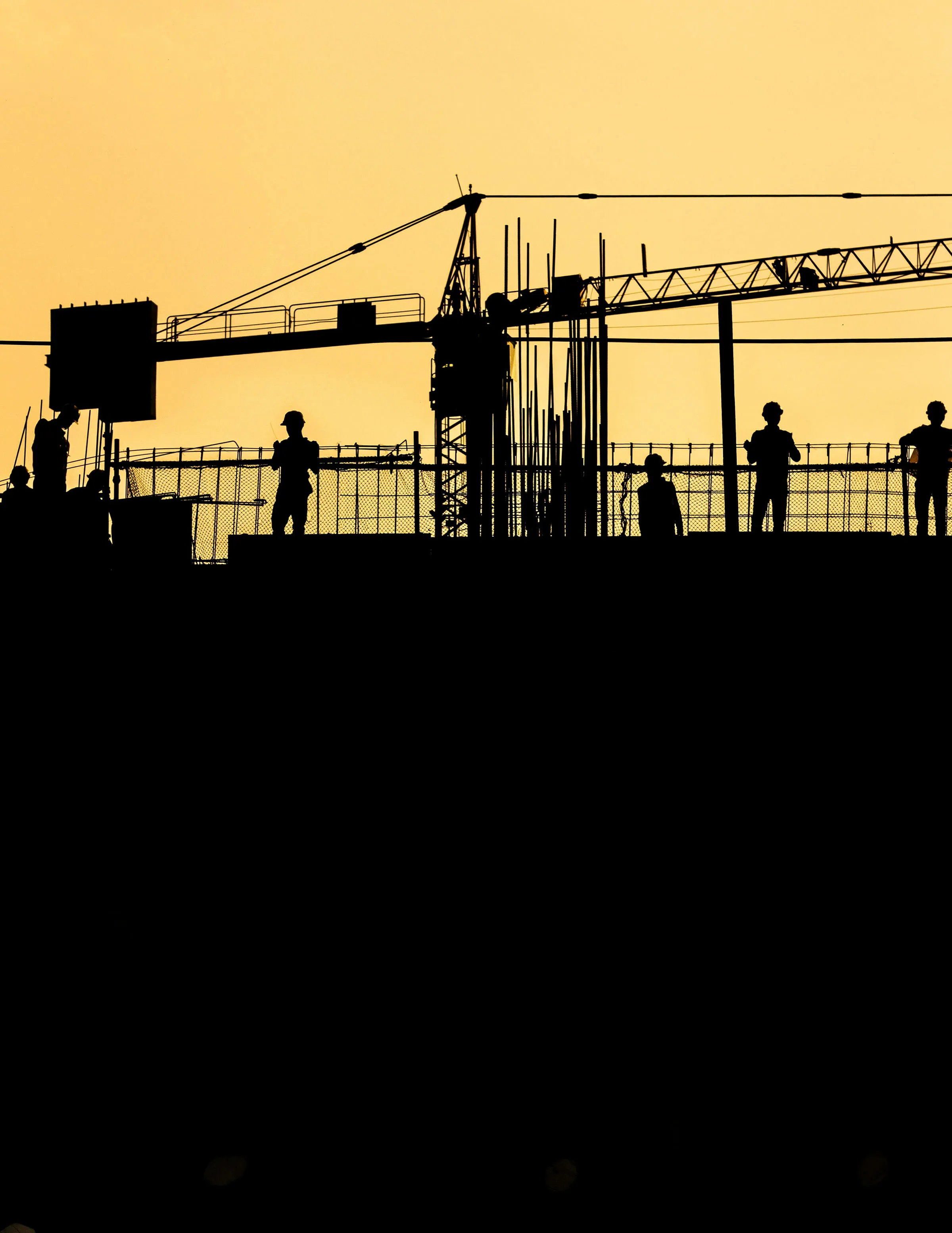 silhouette of men standing on top of building in construction, crane in the background
